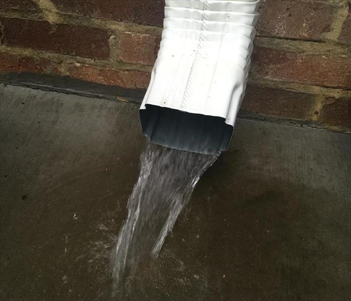 An overflowing gutter and pooling at the bottom of a downspout